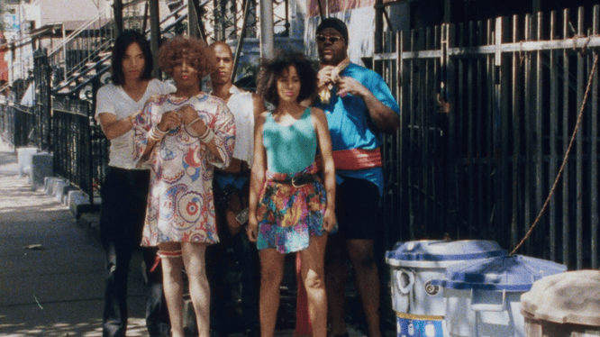 Group of diverse young adults standing outdoors near a fence, with a political message theme.